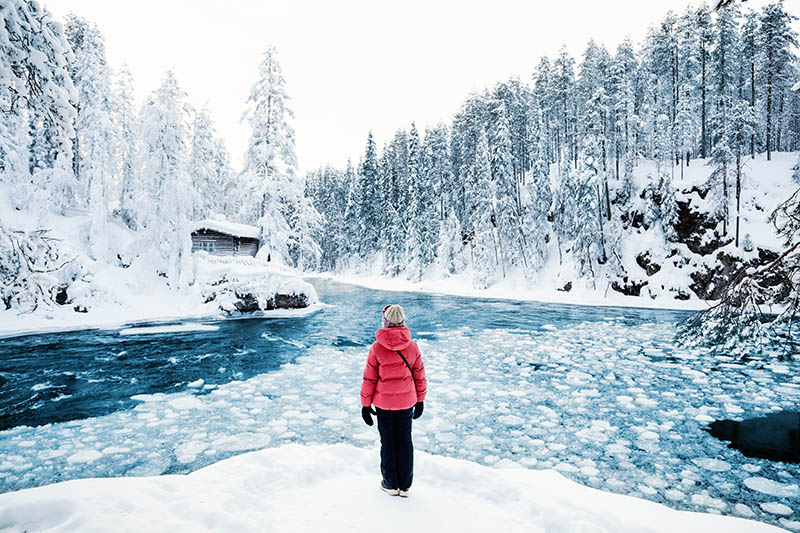Nuori tyttö seisoo talvella osittain sulan joen äärellä.