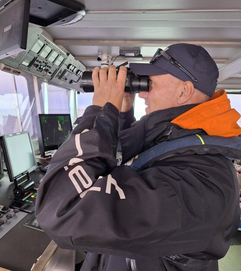 man using binoculars on ship's bridge