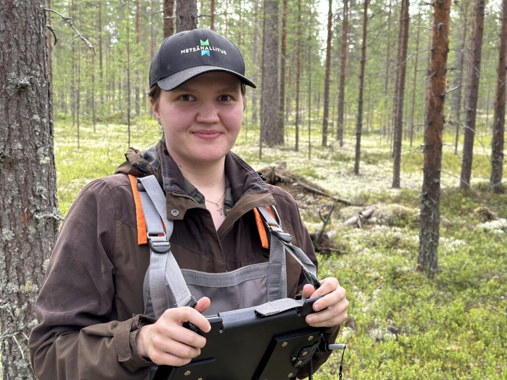 Metsäasiantuntija metsässä maastotietokoneen kanssa.