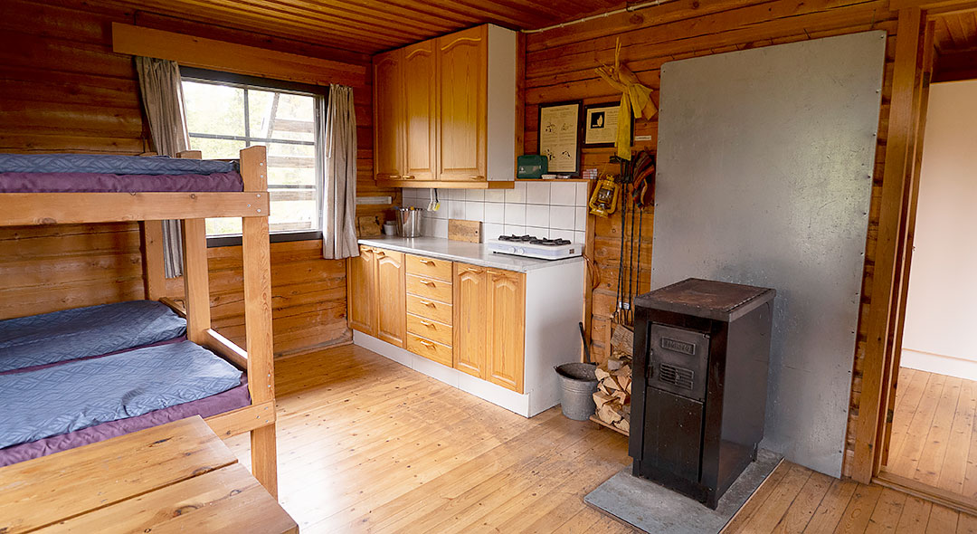 Inside the wooden building, there are loft beds, a kitchen, and a stove.