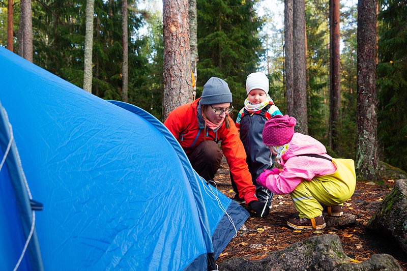 Aikuinen ja lapset pystyttävät telttaa metsään syksyllä.