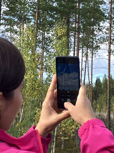 Nainen kuvaa kännykällä tuulivoimalaa.